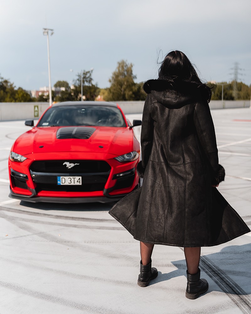 Czarny kożuch damski z kapturem, długim krojem i futrzanym wykończeniem, idealny na zimowe dni